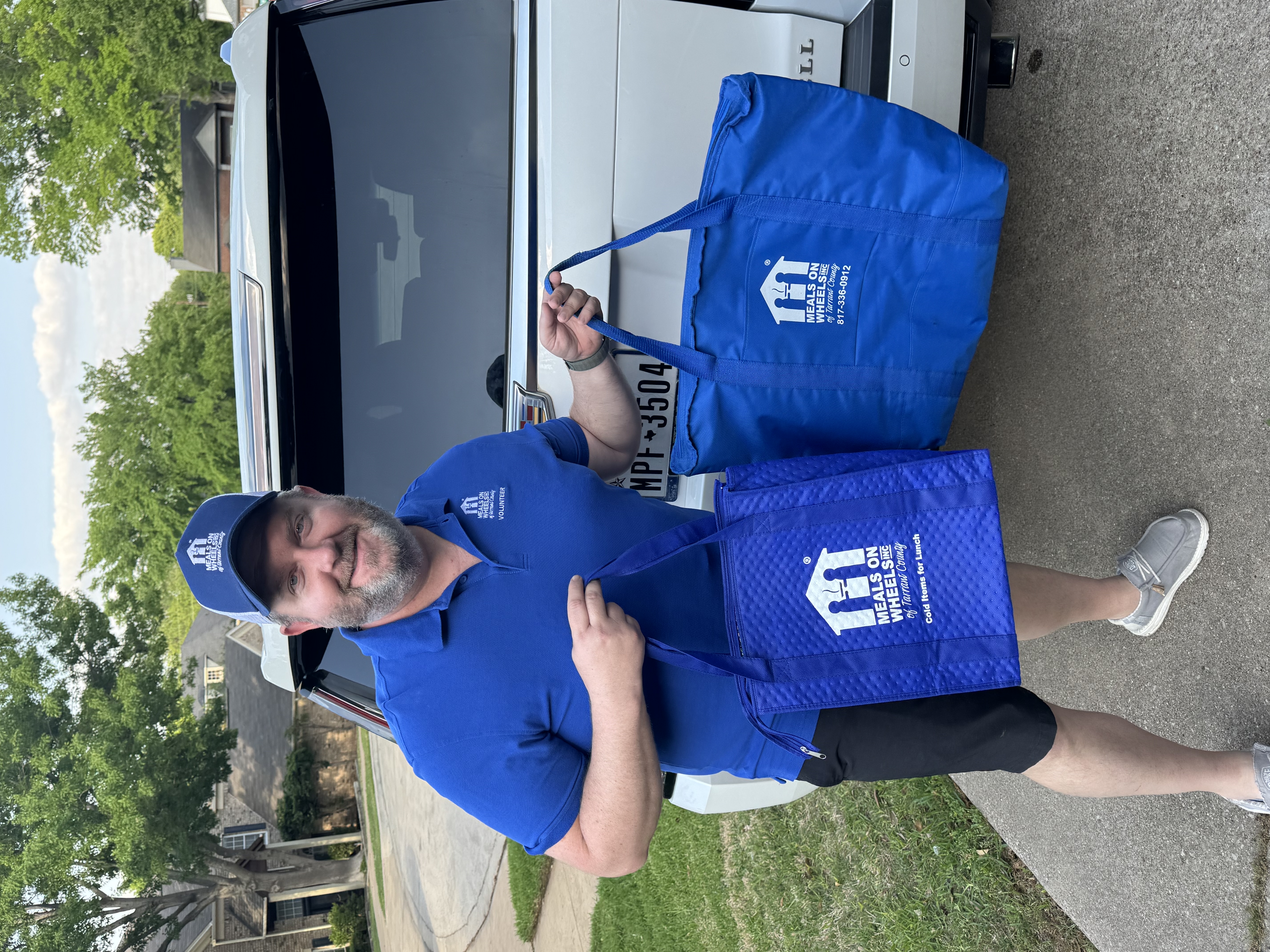 Todd Bingham in his Meals on Wheels volunteer shirt holding insulated delivery bags